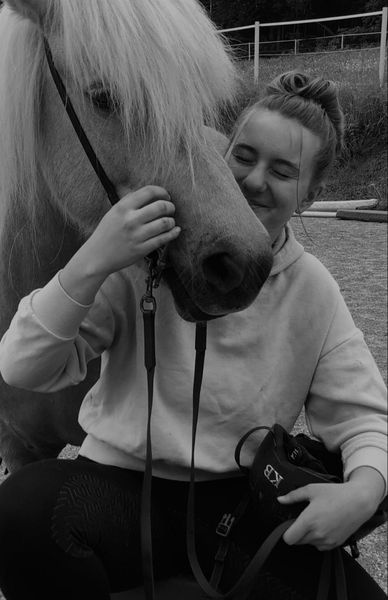 Emma schmiegt sich an ein Pferd und lächelt